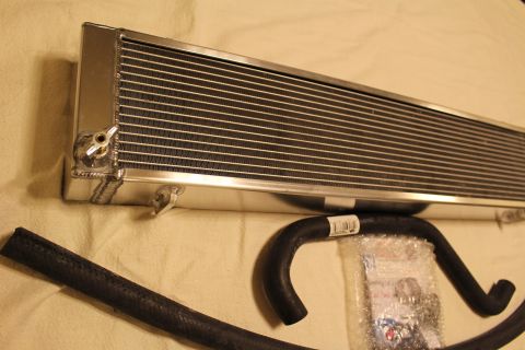 2003 Ford Crown Victoria - aluminum heat exchanger shown at an angle with a brass drain fitting, beside black hoses and a parts bag.