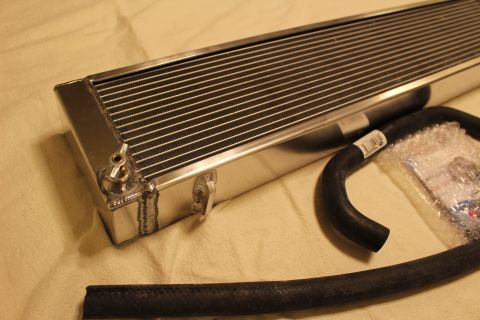 2003 Ford Crown Victoria - Close angled view of an aluminum heat exchanger end with a brass fitting and welds beside a curved black hose.