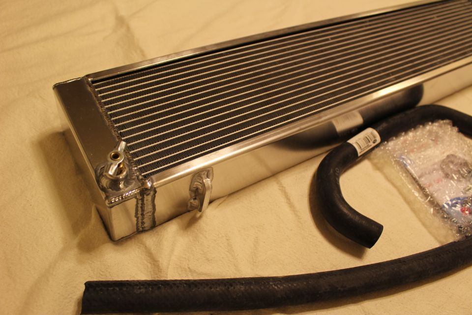 Close-up angled aluminum heat exchanger end with brass fitting beside a black hose
