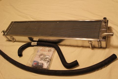 2003 Ford Crown Victoria - aluminum heat exchanger with twin barbed fittings lies above a black coolant hose and a sealed hardware bag.