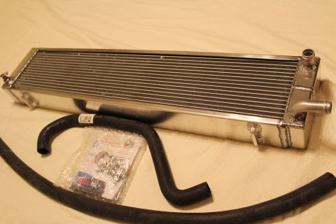 2003 Ford Crown Victoria - aluminum heat exchanger with twin hose barbs is shown above a curved black hose and a clear bag of parts.