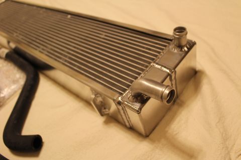 2003 Ford Crown Victoria - Low-angle close-up of an aluminum heat exchanger end tank showing welds and two protruding hose barbs.