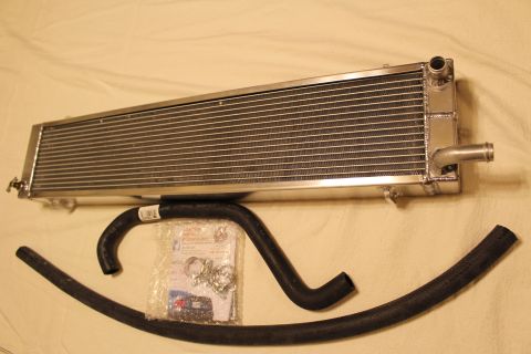 2003 Ford Crown Victoria - aluminum heat exchanger with a hose barb lies above a curved black hose and a sealed bag of clamps and parts.