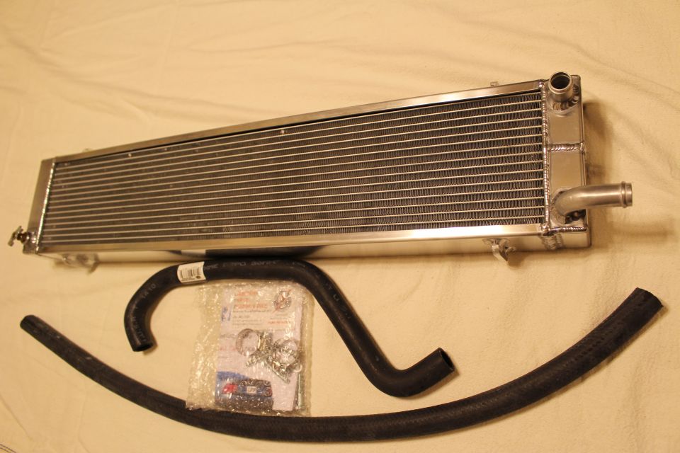 Aluminum heat exchanger with barb fitting above a black hose and hardware bag
