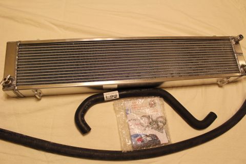 2003 Ford Crown Victoria - aluminum heat exchanger is displayed above a long black coolant hose and a sealed bag of mounting hardware.