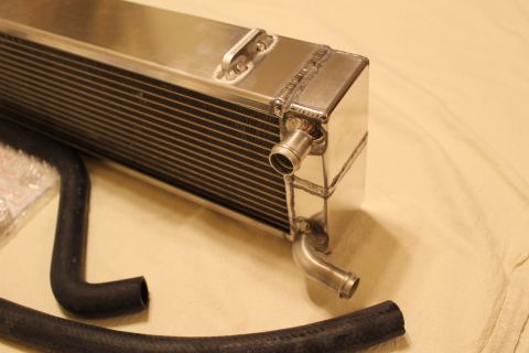 2003 Ford Crown Victoria - Close-up of a polished aluminum heat exchanger's end tank with two hose barb fittings, with a black rubber hose resting on a tan sheet.