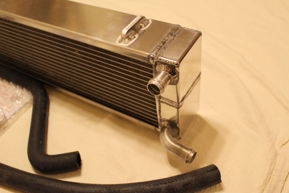 Polished aluminum heat exchanger end tank with inlet/outlet barbs beside black rubber hose