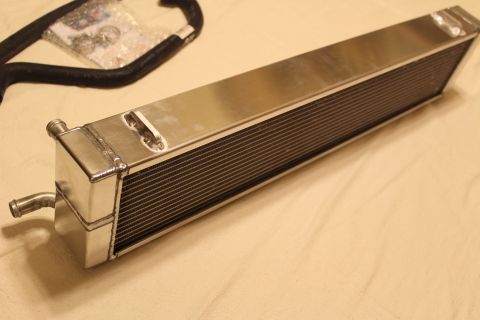2003 Ford Crown Victoria - Angled view of a polished aluminum heat exchanger with an end-tank barb fitting, a black hose and bagged hardware in the background.