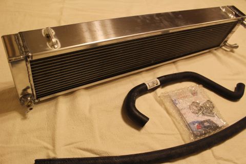 2003 Ford Crown Victoria - polished aluminum heat exchanger sits beside a curved black rubber hose and a bag of clamps and fittings.