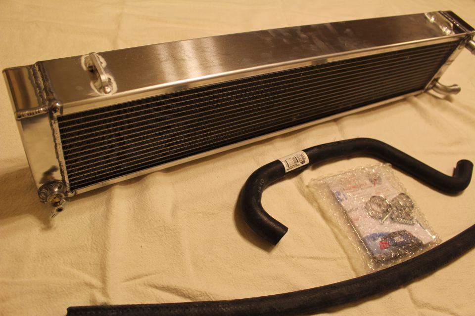 Polished aluminum heat exchanger with black rubber hose and bagged hardware on tan cloth