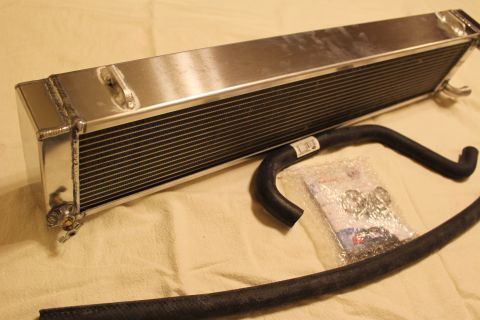 2003 Ford Crown Victoria - polished aluminum heat exchanger laid out with a black rubber hose and a bag of clamps and hardware on a tan sheet.