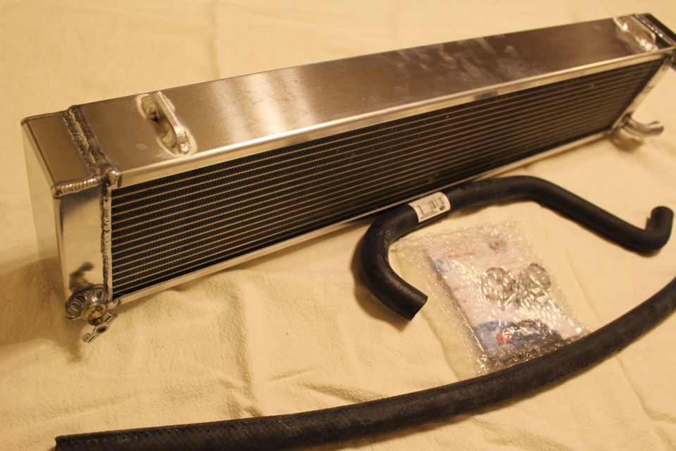 Aluminum heat exchanger with black hose and bagged hardware arranged on tan sheet