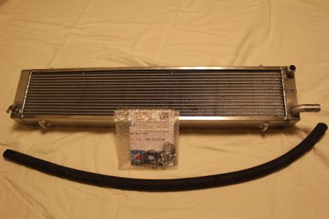 2003 Ford Crown Victoria - polished aluminum heat exchanger with a corner barb fitting, a black rubber hose and a bag of clamps on a tan sheet.