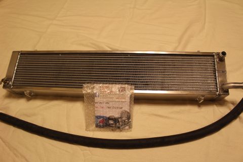 2003 Ford Crown Victoria - long polished aluminum heat exchanger laid flat with a black rubber hose and a bag of fittings and clamps.