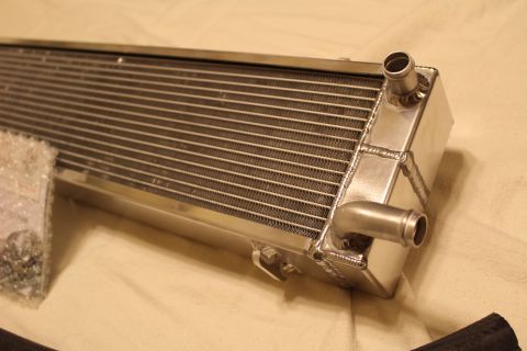 2003 Ford Crown Victoria - Close-up of an aluminum heat exchanger corner showing two hose barb fittings, welded seams and a mounting tab.