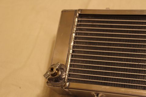 2003 Ford Crown Victoria - Close-up of an aluminum heat exchanger corner showing a small brass fitting, welded seam and the brazed core fins.