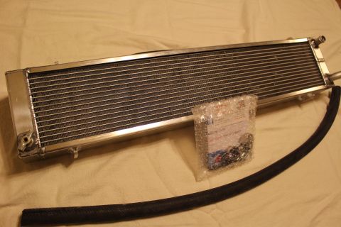 2003 Ford Crown Victoria - polished aluminum heat exchanger laid flat with a bubble-wrapped bag of hardware and a coiled black hose.