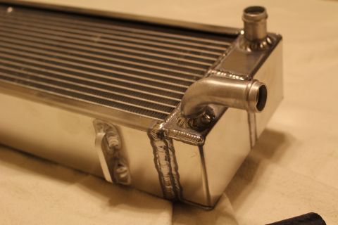 2003 Ford Crown Victoria - Close-up of an aluminum heat exchanger end tank showing two angled hose barb fittings and heavy welded seams.