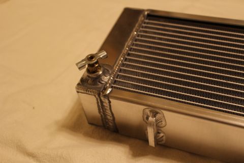 2003 Ford Crown Victoria - Close-up of an aluminum heat exchanger corner showing a small brass petcock-style fitting and welded seams.