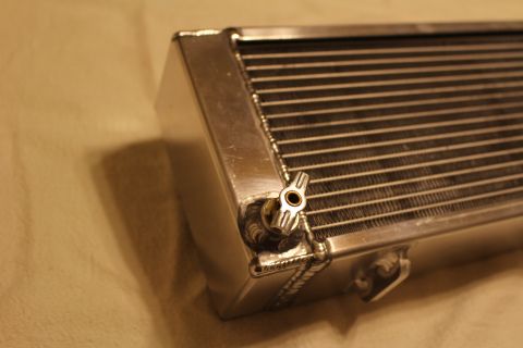 2003 Ford Crown Victoria - Close-up of an aluminum heat exchanger end showing a small brass drain fitting, welded seams and brazed core fins.