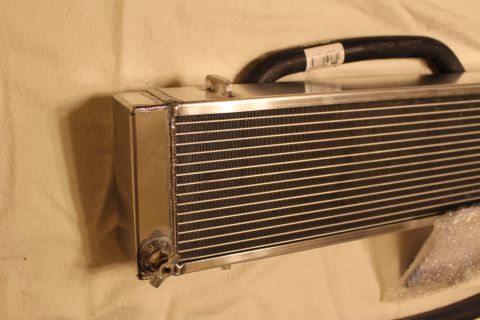 2003 Ford Crown Victoria - aluminum heat exchanger end with a small brass fitting, a coiled black hose behind it and bubble wrap on a tan cloth.