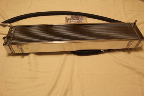 2003 Ford Crown Victoria - polished aluminum heat exchanger lying flat with a long curved black hose draped above it and a bag of hardware.