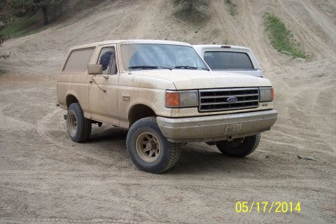 1990 Ford Bronco - This 1990 Ford Bronco is seen in a dusty, off-road environment with another vehicle partially visible behind it.