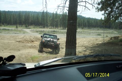 1990 Ford Bronco - A Jeep Wrangler navigates an off-road trail with a wooded area behind it.