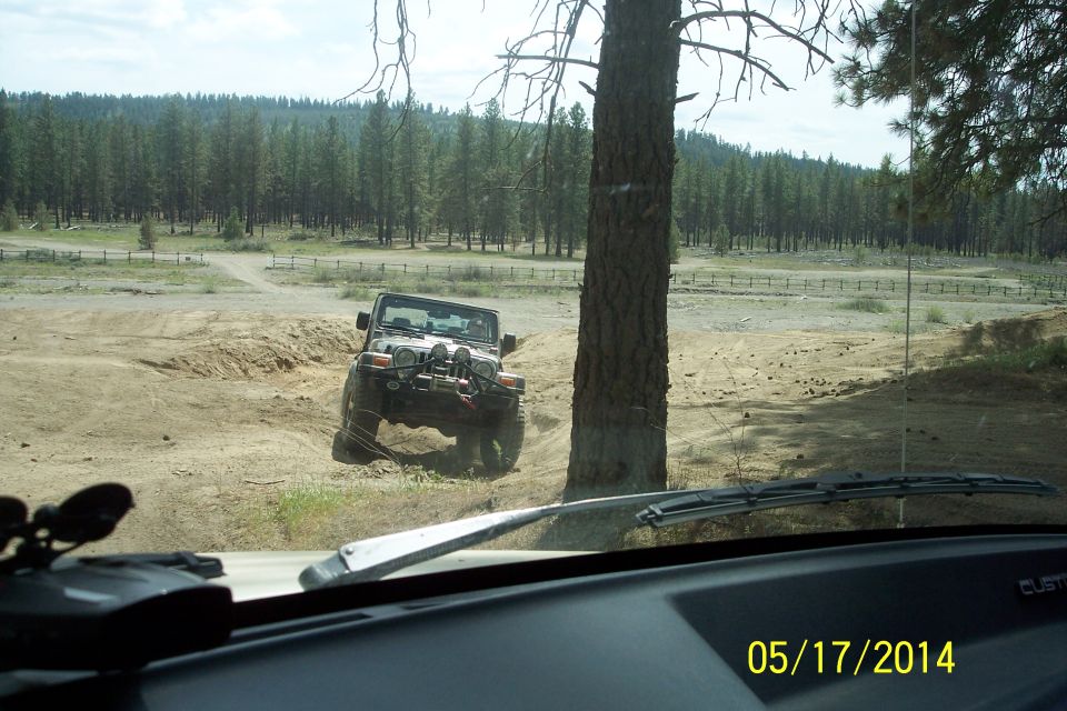 Jeep Wrangler driving on a dirt path with trees and a fence in the background