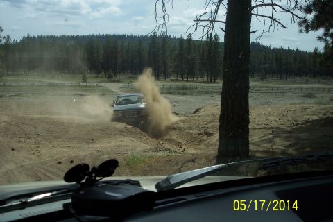 1990 Ford Bronco - A silver Ford Bronco drives off-road, kicking up a large dust cloud.