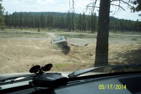 1990 Ford Bronco - A white 1990 Ford Bronco navigates a challenging off-road course, kicking up dust as it maneuvers through the terrain.