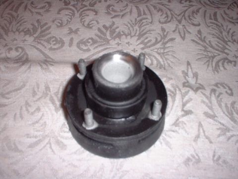1996 Ford Taurus - A car strut mount is shown against a patterned fabric background. The part has four bolts protruding from its base.