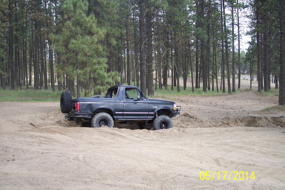 1990 Ford Bronco driving through sand with trees in background