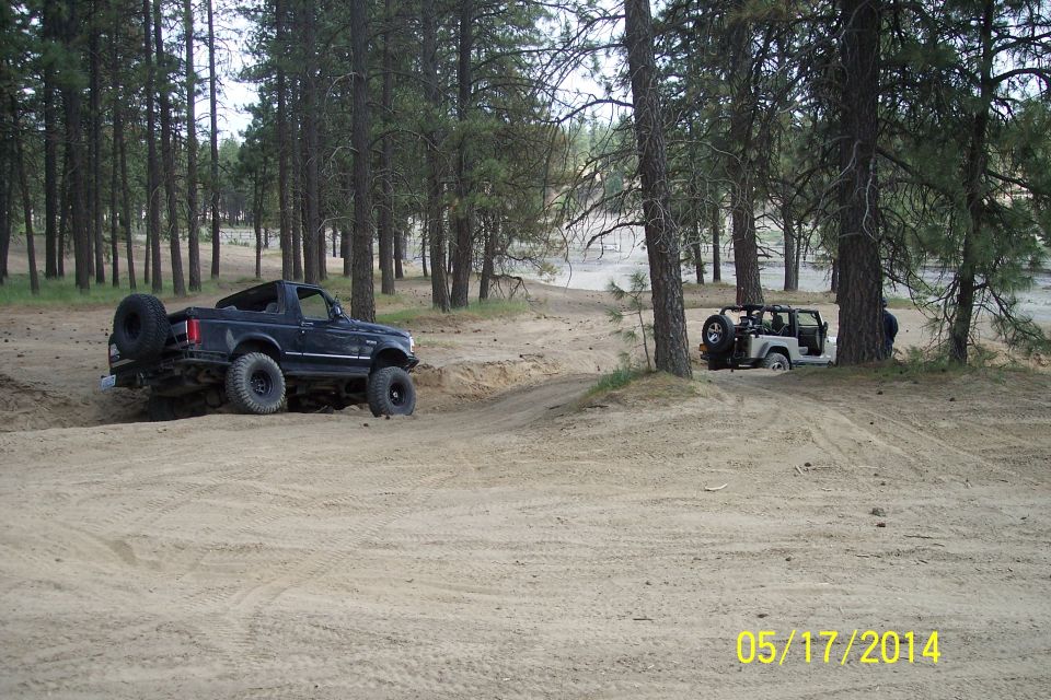Black Ford Bronco and white Jeep Wrangler driving on a dirt path in a forest