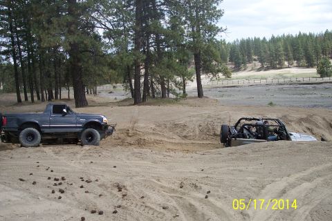 1990 Ford Bronco - Two off-road vehicles are stuck in the sand, one a dark blue pickup truck and the other a partially submerged buggy.