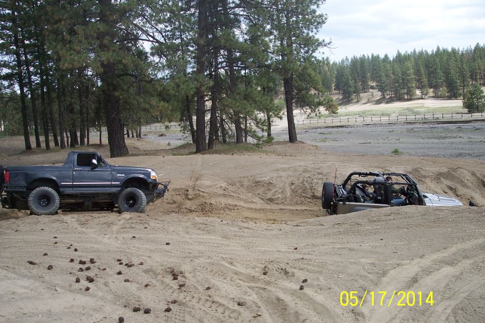 Dark blue pickup truck with off-road tires stuck in sand, another vehicle partially submerged