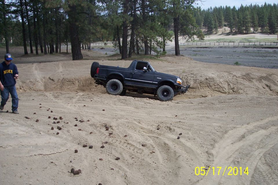 Black 1990 Ford Bronco driving on a sandy hill with a person standing nearby