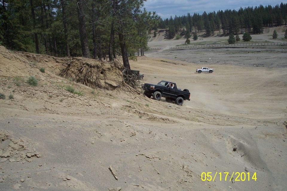 Black 1990 Ford Bronco climbing a dirt hill, white truck in background