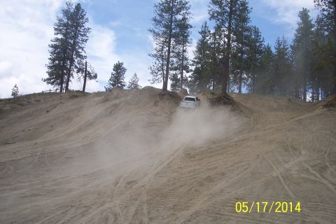 1990 Ford Bronco - A white pickup truck navigates a dusty off-road hill, surrounded by pine trees and a cloudy sky.