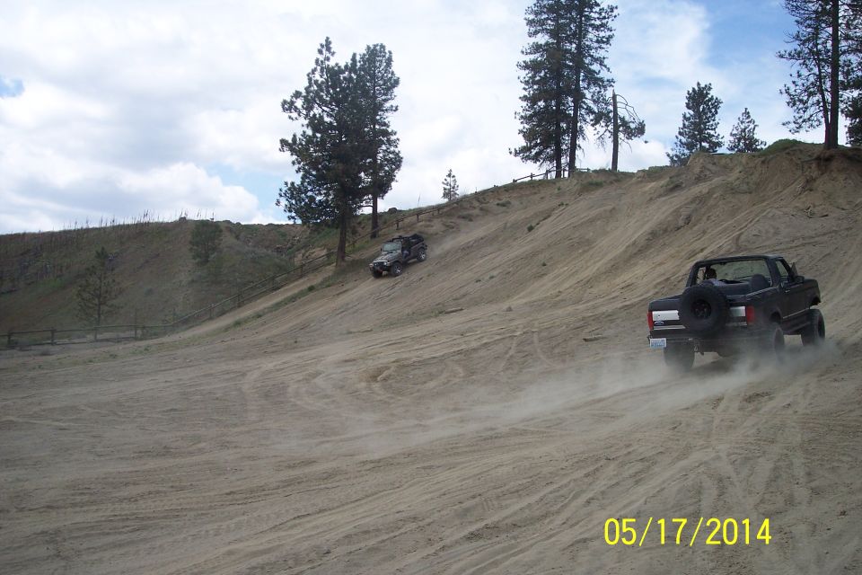 Black Ford Bronco with spare tire on rear, kicking up dust on a sandy hill