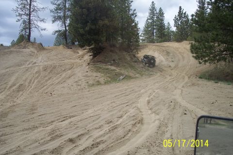 1990 Ford Bronco - An off-road vehicle navigates a challenging sandy terrain with pine trees overhead.