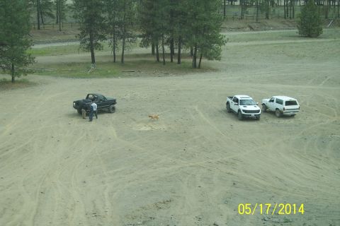 1990 Ford Bronco - Three vehicles and a dog are gathered in a dusty, open area with trees in the distance.
