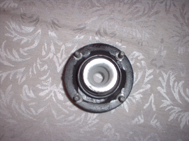 Strut mount with four bolts on a patterned fabric background. Text 'SUPERMOTORS' is visible