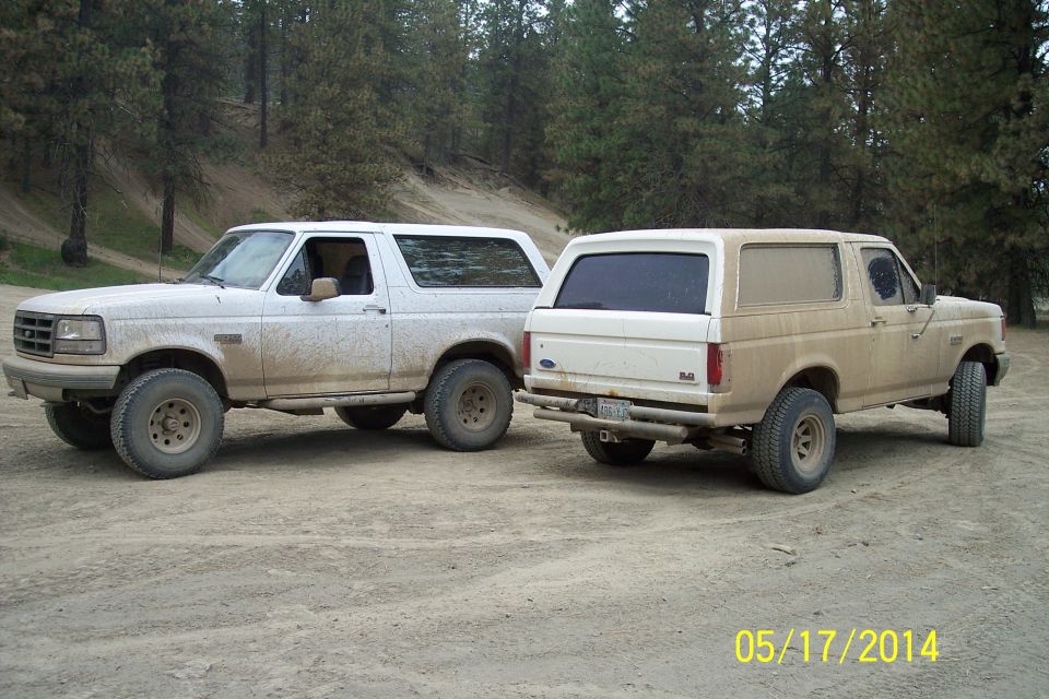 Two white Ford Broncos parked on a dirt road, one facing front, the other rear