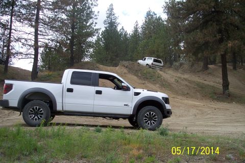 1990 Ford Bronco - Two trucks are seen off-roading on a dirt hill with trees surrounding the area.