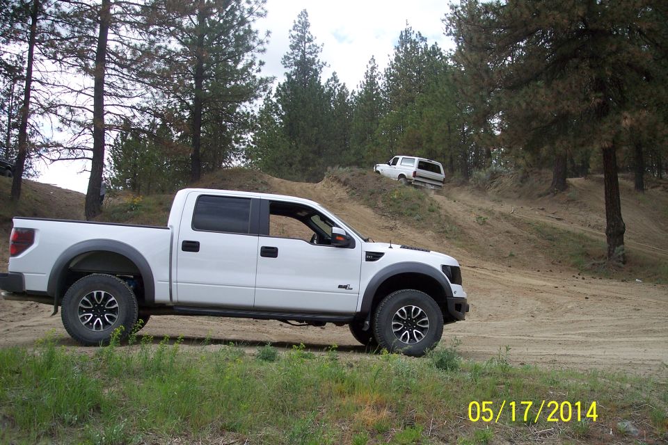 White pickup truck in foreground, white SUV climbing dirt hill in background