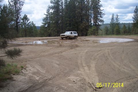 1990 Ford Bronco - A white SUV navigates a muddy off-road area with several puddles under a cloudy sky.