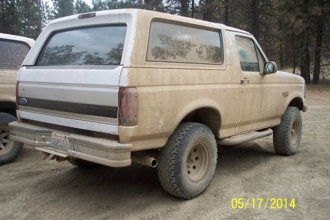 1990 Ford Bronco - This 1990 Ford Bronco is heavily coated in mud, seen from the rear with another vehicle in the background.
