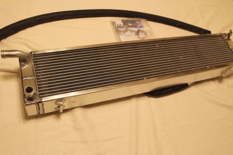 2003 Ford Crown Victoria - polished aluminum heat exchanger laid flat with an end barb fitting, a curved black hose and a bag of hardware.