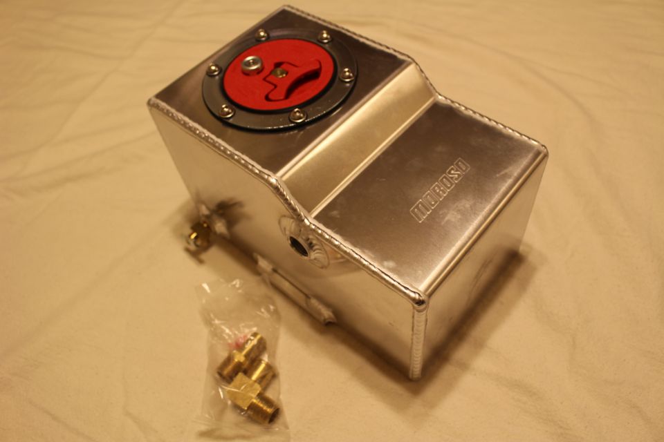 Polished aluminum reservoir tank with red flush cap and brass fittings on tan cloth
